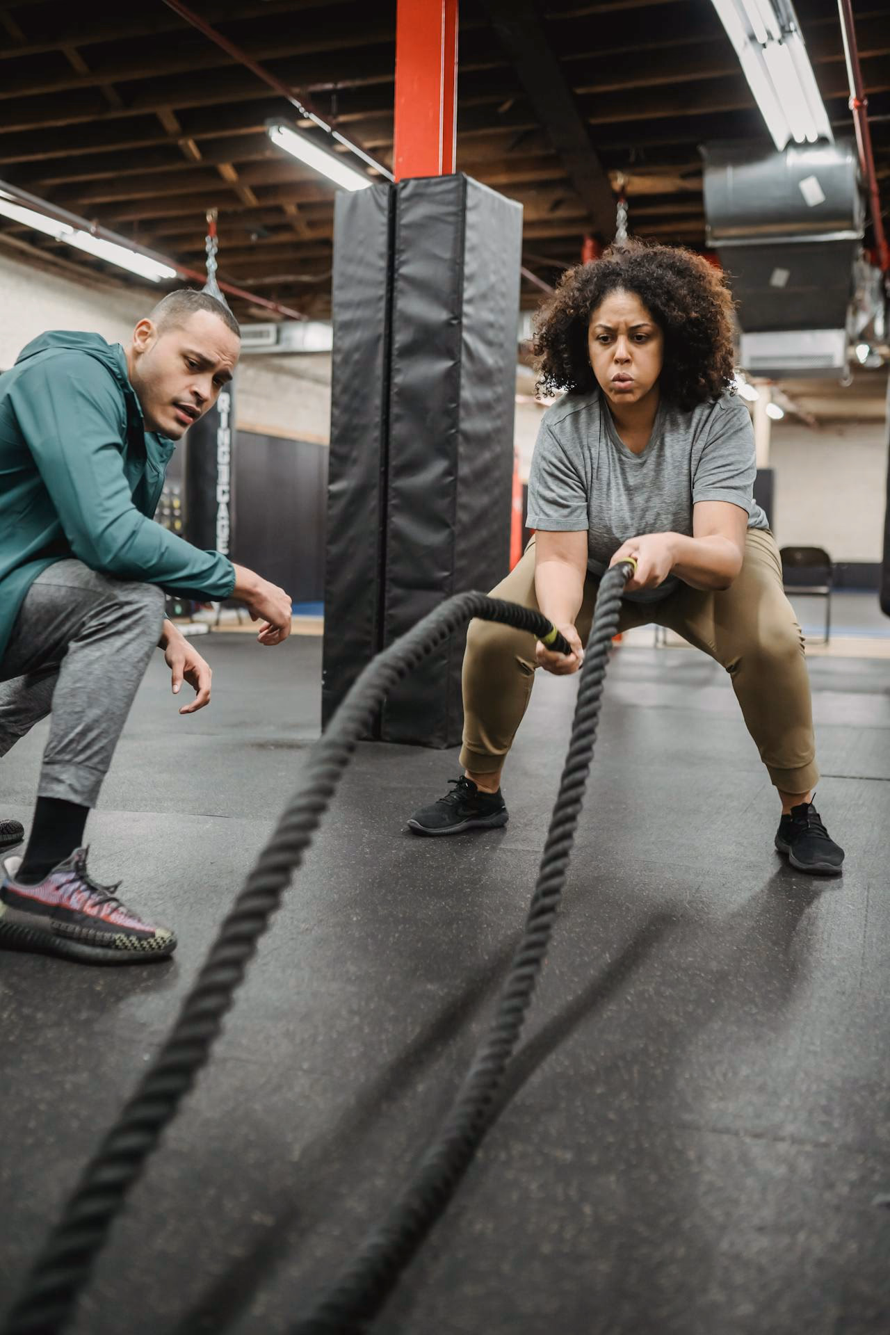 Concentrated black woman exercising with battle ropes in contemporary gym